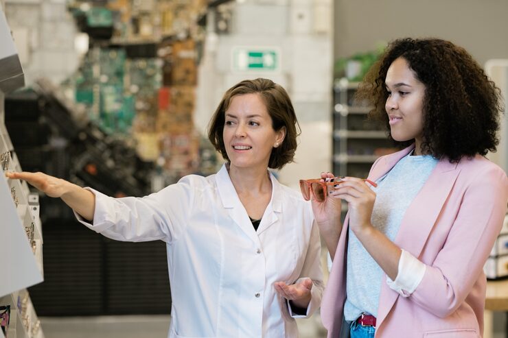 confident-young-consultant-whitecoat-showing-female-client-new-models-eyeglasses-display_274679-7011