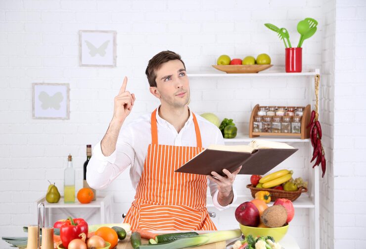 man-with-recipe-book-hands-table-with-different-products-utensil-kitchen-white-wall-background_392895-198180